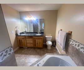 Full bath with double vanity, a whirlpool tub, and light tile patterned floors