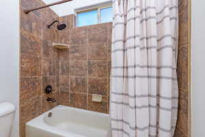 Full bathroom featuring shower / bath combination with curtain and toilet