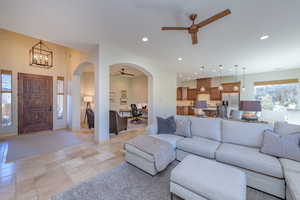 Living room with ceiling fan, a desk, arched walkways, recessed lighting, and light stone finish flooring