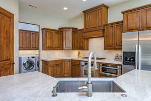 Kitchen featuring appliances with stainless steel finishes, brown cabinets, backsplash, recessed lighting, and washing machine and clothes dryer