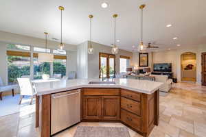 Kitchen featuring brown cabinetry, hanging light fixtures, stainless steel dishwasher, a kitchen island with sink, and recessed lighting