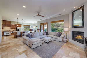 Living room featuring recessed lighting, healthy amount of natural light, a ceiling fan, a glass covered fireplace, and stone tile flooring