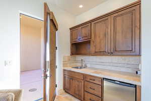 Kitchen with tasteful backsplash, stainless steel dishwasher, brown cabinetry, light tile patterned floors, and recessed lighting