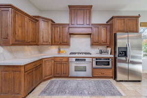 Kitchen with stainless steel appliances, brown cabinets, backsplash, and stone tile flooring