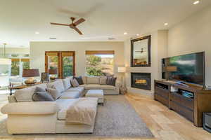 Living area with ceiling fan, recessed lighting, a glass covered fireplace, and stone tile floors