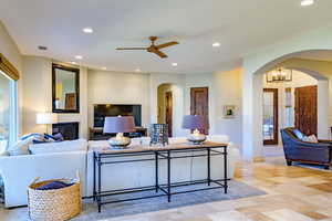 Living room with arched walkways, recessed lighting, a glass covered fireplace, ceiling fan, and stone tile flooring
