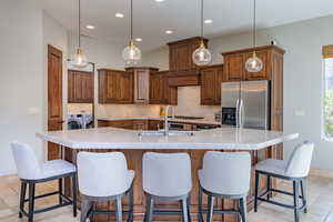 Kitchen featuring stainless steel fridge, brown cabinets, tasteful backsplash, a breakfast bar area, and recessed lighting