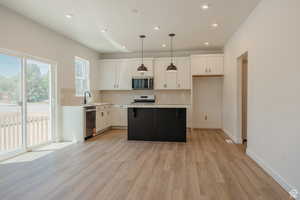 Kitchen featuring backsplash, white cabinets, hanging light fixtures, a kitchen island, and light wood finished floors