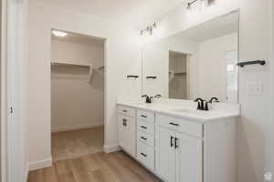Bathroom with a spacious closet, light wood-style floors, and double vanity