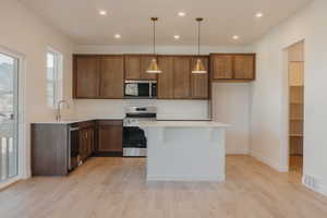 Kitchen with pendant lighting, recessed lighting, appliances with stainless steel finishes, a kitchen breakfast bar, and light wood-style floors