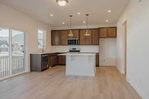 Kitchen with decorative light fixtures, recessed lighting, light wood-style flooring, a kitchen island, and stainless steel appliances