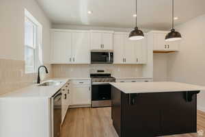 Kitchen with stainless steel appliances, white cabinets, decorative light fixtures, backsplash, and a center island