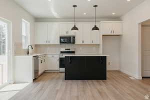 Kitchen featuring white cabinets, backsplash, decorative light fixtures, light wood-style floors, and recessed lighting