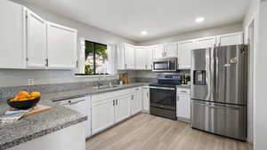 Kitchen with appliances with stainless steel finishes, white cabinets, light stone countertops, light wood-style flooring, and recessed lighting