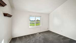 Spare room featuring dark carpet and baseboards