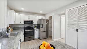 Kitchen with stainless steel appliances, white cabinetry, light wood-type flooring, recessed lighting, and light stone countertops