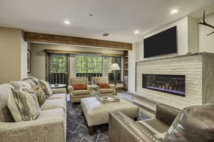 Living room featuring wood finished floors, a glass covered fireplace, recessed lighting, and beam ceiling