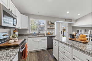Kitchen with appliances with stainless steel finishes, dark wood finished floors, white cabinets, recessed lighting, and light stone countertops