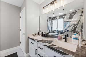 Bathroom with a marble finish shower, double vanity, and light tile patterned floors