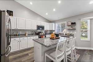 Kitchen with dark stone countertops, a breakfast bar, dark wood-style flooring, stainless steel appliances, and vaulted ceiling