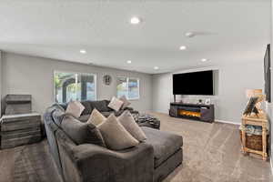 Carpeted living area featuring healthy amount of natural light, recessed lighting, a textured ceiling, and a lit fireplace
