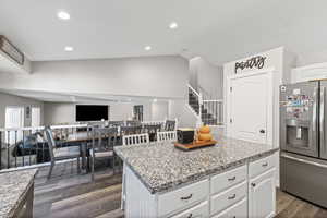 Kitchen featuring vaulted ceiling, white cabinetry, stainless steel fridge, recessed lighting, and dark wood finished floors