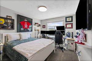 Carpeted bedroom featuring a textured ceiling and a desk
