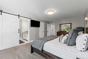 Bedroom featuring a textured ceiling, carpet floors, ensuite bath, and a barn door