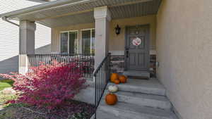 View of exterior entry featuring covered porch, stucco siding, and stone siding