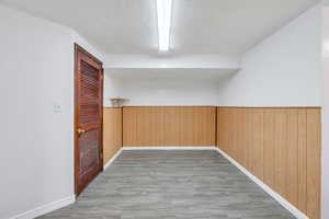 Unfurnished room with a wainscoted wall, light wood-style flooring, wooden walls, and a textured ceiling