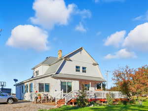 Rear view of property featuring a lawn, a chimney, a gambrel roof, and a wooden deck