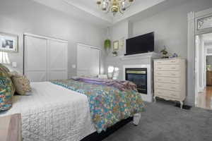 Carpeted bedroom with two closets, a glass covered fireplace, and a chandelier