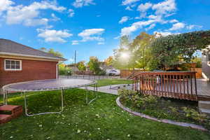 View of yard featuring a trampoline, a deck, and a patio