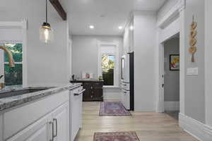 Kitchen featuring white cabinets, light stone counters, light wood-style flooring, high end refrigerator, and recessed lighting