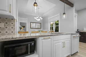 Kitchen with white cabinetry, black microwave, light stone counters, hanging light fixtures, and beamed ceiling