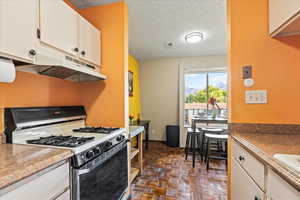 Kitchen featuring gas range gas stove, a textured ceiling, under cabinet range hood, and cream cabinetry