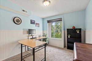 Office area featuring a wainscoted wall, light carpet, and a textured ceiling