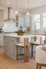 Kitchen featuring light wood-type flooring, a breakfast bar area, decorative light fixtures, and tasteful backsplash