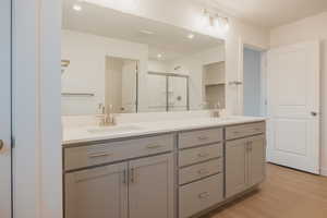 Full bath featuring a stall shower, double vanity, light wood finished floors, and recessed lighting