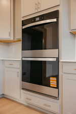 Kitchen view of stainless steel double oven, white cabinetry, light wood-style flooring, and tasteful backsplash