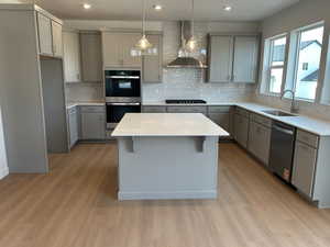 Kitchen featuring gray cabinetry, hanging light fixtures, a breakfast bar area, tasteful backsplash, and wall chimney range hood