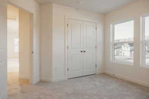 Unfurnished bedroom with light colored carpet, a closet, and multiple windows