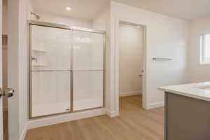 Full bath featuring vanity, light wood finished floors, a stall shower, and a walk in closet