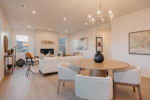 Dining room with light wood-type flooring, a large fireplace, and suspended lighting
