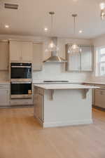 Kitchen featuring decorative light fixtures, tasteful backsplash, double oven, gray cabinets, and a breakfast bar area