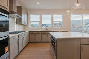 Kitchen featuring light wood-style floors, pendant lighting, appliances with stainless steel finishes, wall chimney exhaust hood, and decorative backsplash