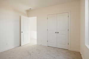 Unfurnished bedroom featuring light carpet and a closet