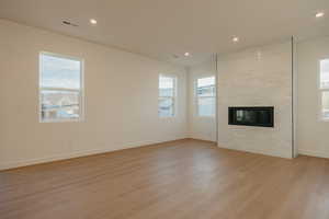 Unfurnished living room featuring light wood finished floors, a brick fireplace, and recessed lighting