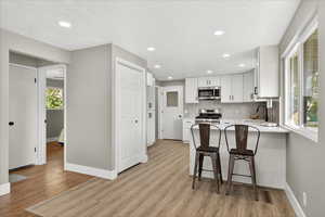 Kitchen featuring white cabinetry, a breakfast bar area, stainless steel appliances, light wood finished floors, and backsplash