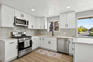 Kitchen with stainless steel appliances, white cabinets, light wood-type flooring, recessed lighting, and light stone countertops